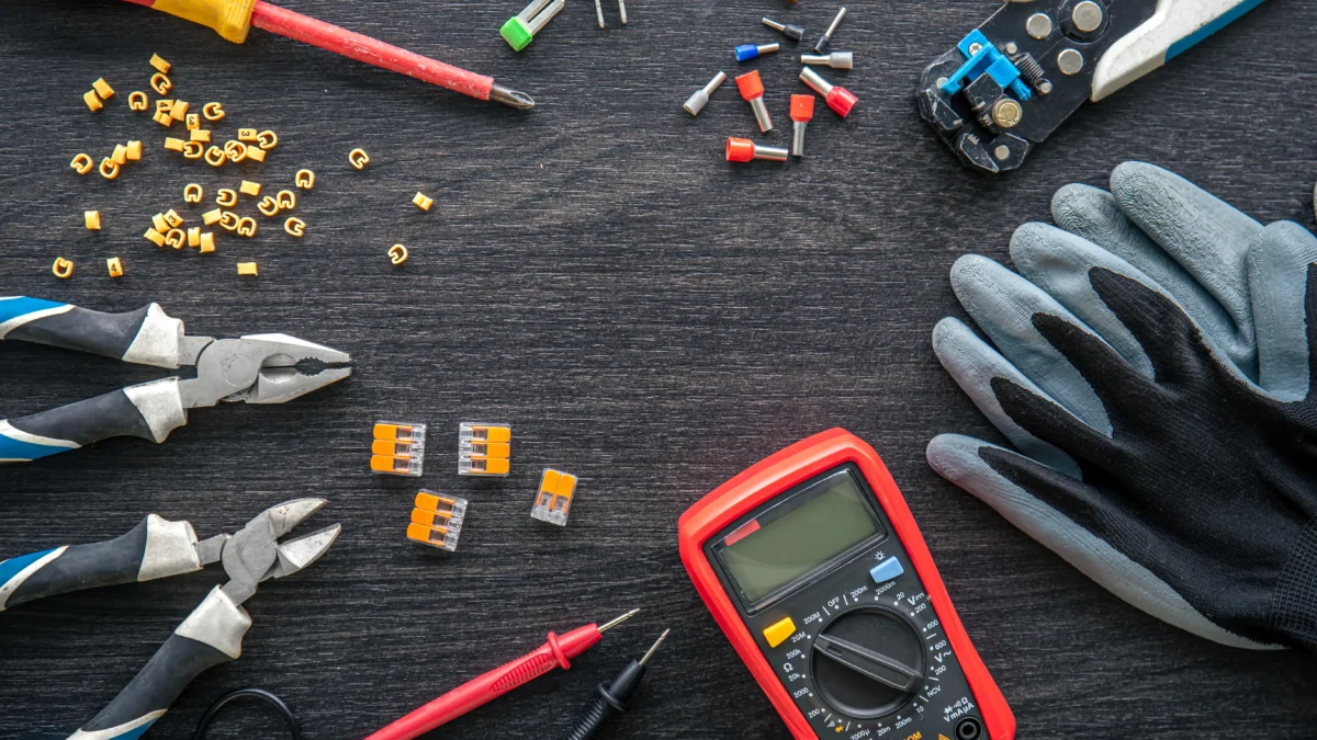 Ferramentas de eletricista organizadas sobre uma mesa: multímetro, alicates, chave de fenda, luvas e conectores elétricos.