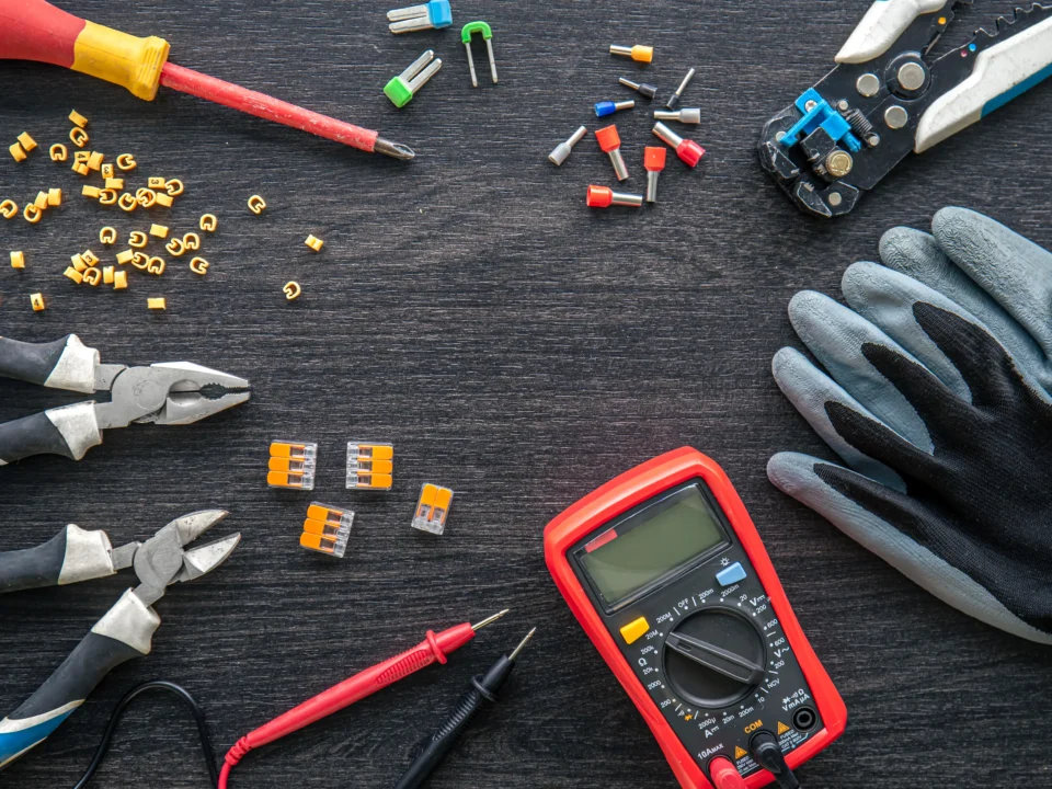 Ferramentas de eletricista organizadas sobre uma mesa: multímetro, alicates, chave de fenda, luvas e conectores elétricos.