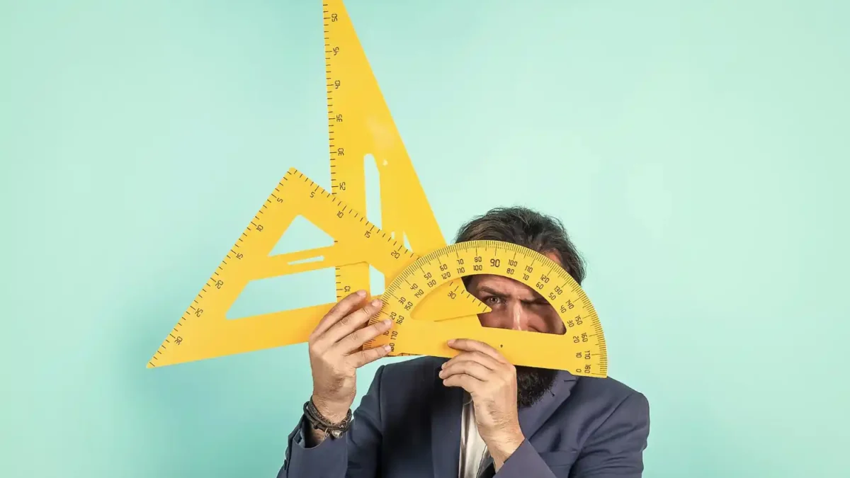 Homem de terno cobrindo o rosto com grandes ferramentas de geometria amarelas.