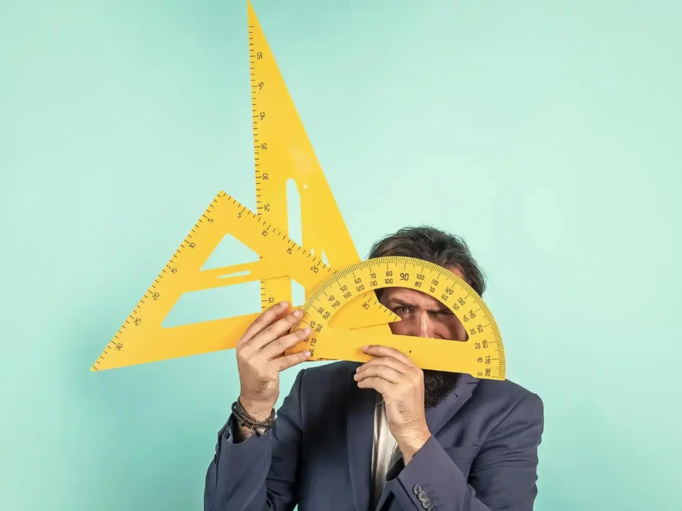 Homem de terno cobrindo o rosto com grandes ferramentas de geometria amarelas.