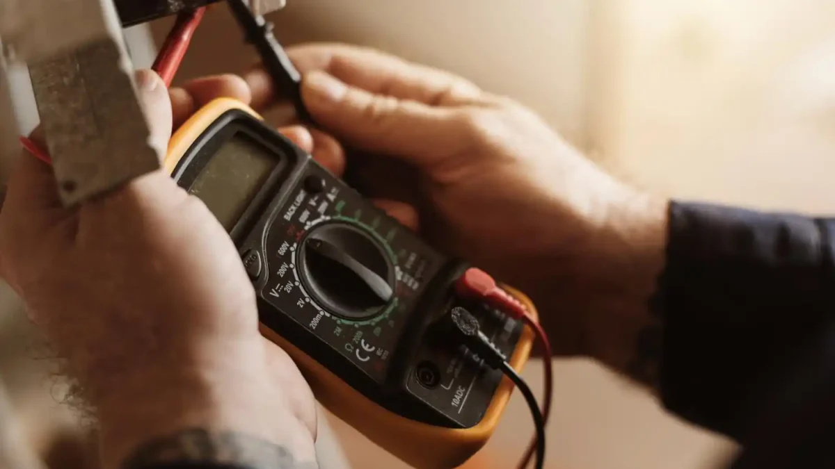 Pessoa usando multímetro digital para medir tensão elétrica em fios, em ambiente interno.
