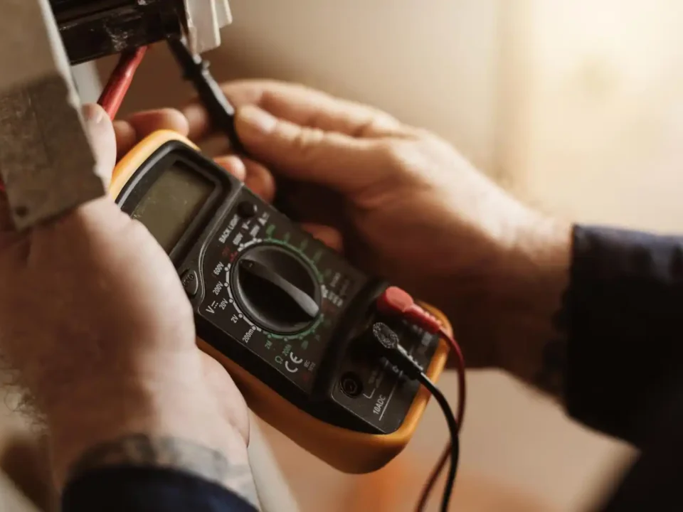 Pessoa usando multímetro digital para medir tensão elétrica em fios, em ambiente interno.