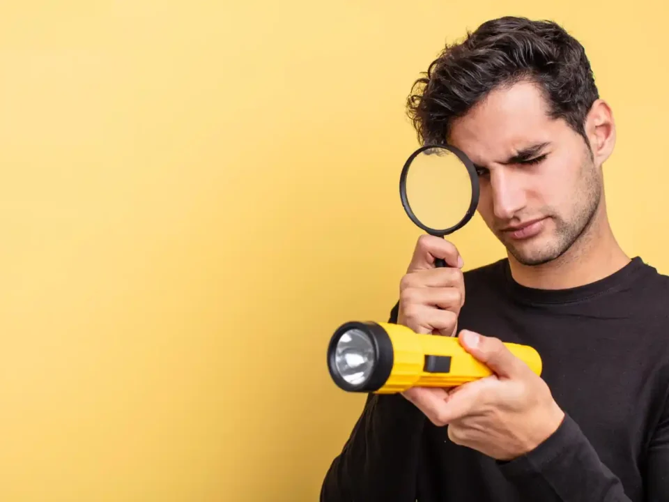 Homem examinando uma lanterna amarela com uma lupa sobre fundo amarelo.